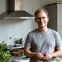 Hombre de mediana edad con una sonrisa confiada, parado en una cocina moderna preparando una ensalada.