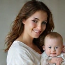 Joven madre sosteniendo a su bebé y sonriendo, con un brillo saludable.